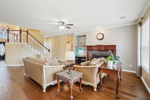 living room featuring dark hardwood / wood-style floors, ornamental molding, a fireplace, and ceiling fan with notable chandelier