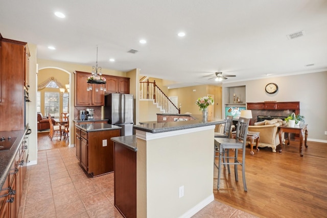 kitchen featuring a breakfast bar, ceiling fan, light tile patterned floors, a center island, and stainless steel refrigerator