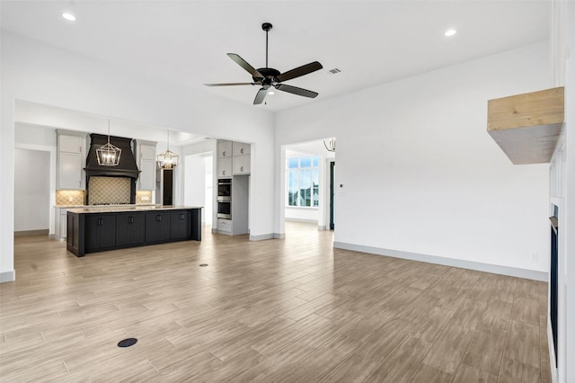 unfurnished living room with ceiling fan with notable chandelier, a fireplace, and light hardwood / wood-style floors