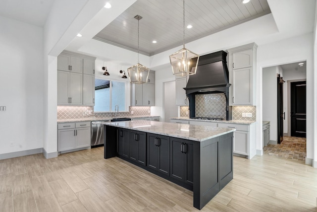 kitchen with a raised ceiling, hanging light fixtures, a center island, and custom range hood