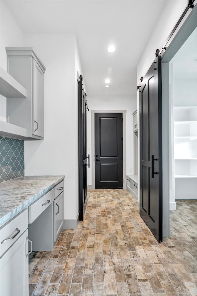 kitchen featuring light stone countertops, a barn door, gray cabinetry, and decorative backsplash