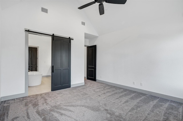 unfurnished bedroom with ensuite bathroom, high vaulted ceiling, ceiling fan, a barn door, and light carpet