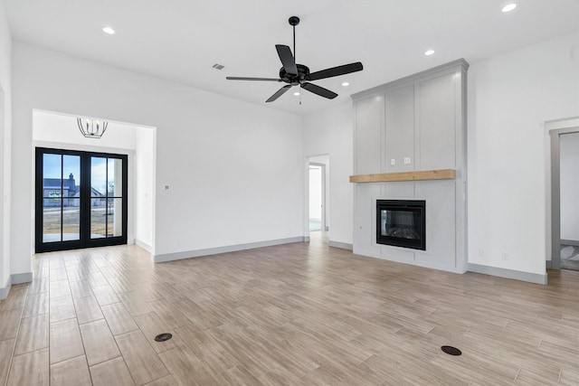 unfurnished living room featuring ceiling fan with notable chandelier, a fireplace, light hardwood / wood-style floors, and french doors