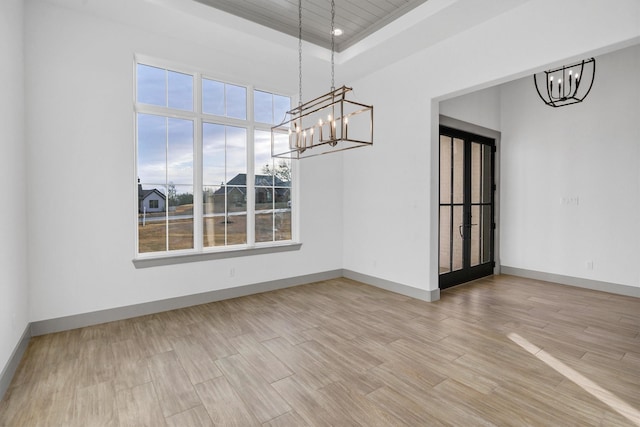 unfurnished dining area featuring an inviting chandelier, a tray ceiling, and light hardwood / wood-style floors