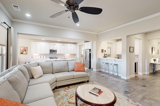 living room featuring light hardwood / wood-style flooring, ceiling fan, crown molding, and sink