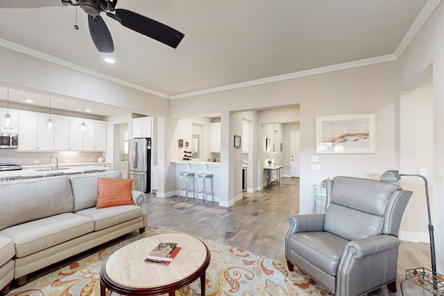 living room featuring ceiling fan, ornamental molding, sink, and light wood-type flooring