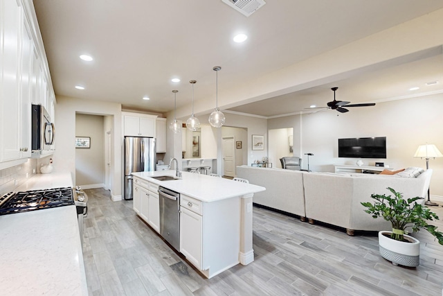 kitchen featuring white cabinets, hanging light fixtures, sink, an island with sink, and appliances with stainless steel finishes