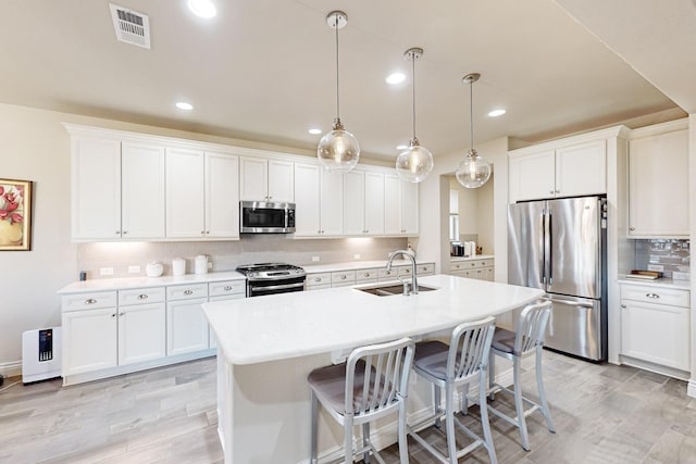 kitchen featuring sink, white cabinets, hanging light fixtures, stainless steel appliances, and a center island with sink