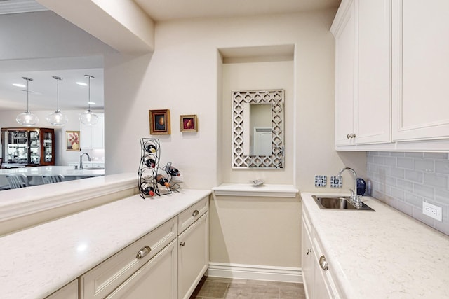 kitchen featuring backsplash, decorative light fixtures, white cabinetry, and sink