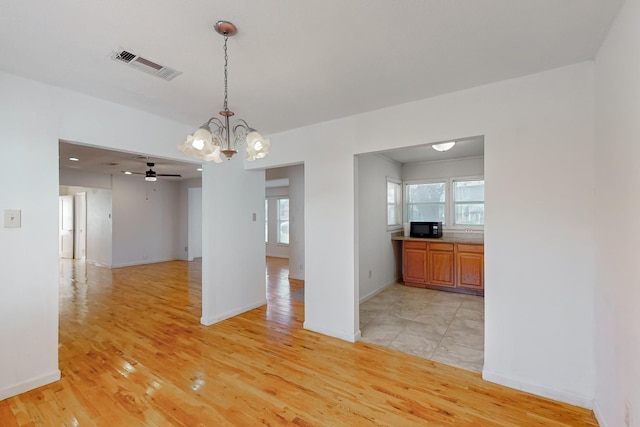 empty room with light hardwood / wood-style flooring and ceiling fan with notable chandelier