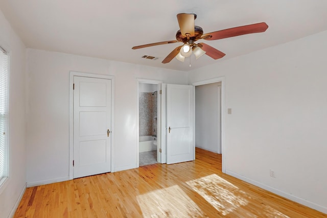 unfurnished bedroom featuring light wood-type flooring, connected bathroom, multiple windows, and ceiling fan