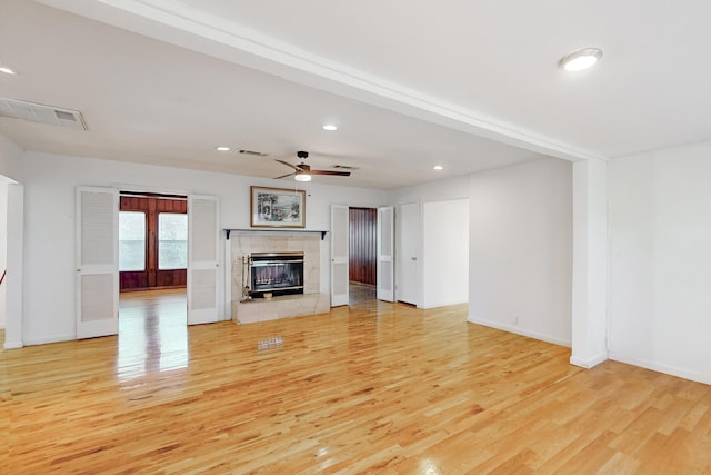 unfurnished living room featuring light wood-type flooring, ceiling fan, and a tiled fireplace