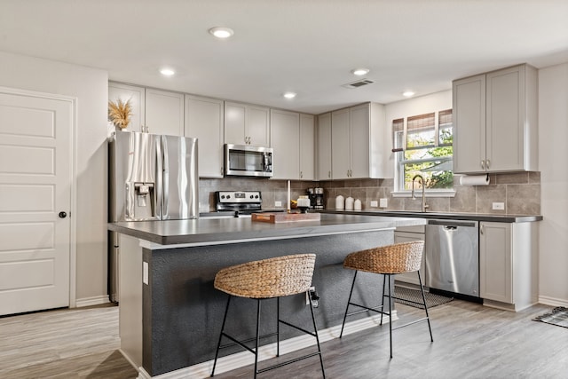 1813 Aslynn Cir, Aubrey, TX 76227 - kitchen with appliances with stainless steel finishes, a kitchen breakfast bar, light wood-type flooring, backsplash, and a center island