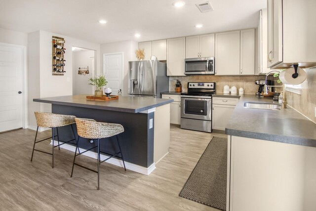 kitchen featuring stainless steel appliances, backsplash, a breakfast bar area, a kitchen island, and light wood-type flooring