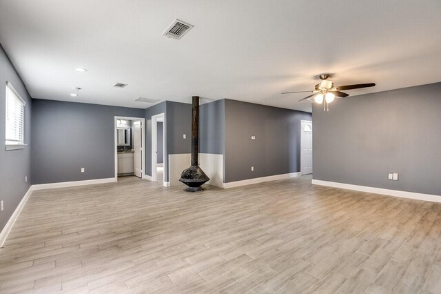 unfurnished living room featuring ceiling fan, light wood-type flooring, and a wood stove