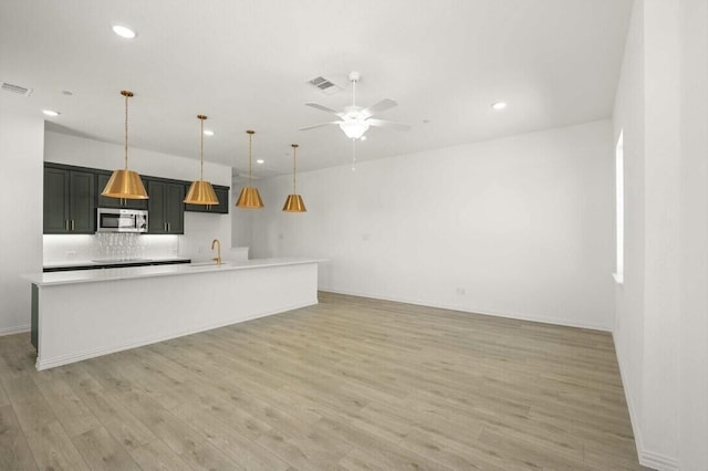 kitchen with light wood finished floors, visible vents, stainless steel microwave, and a sink