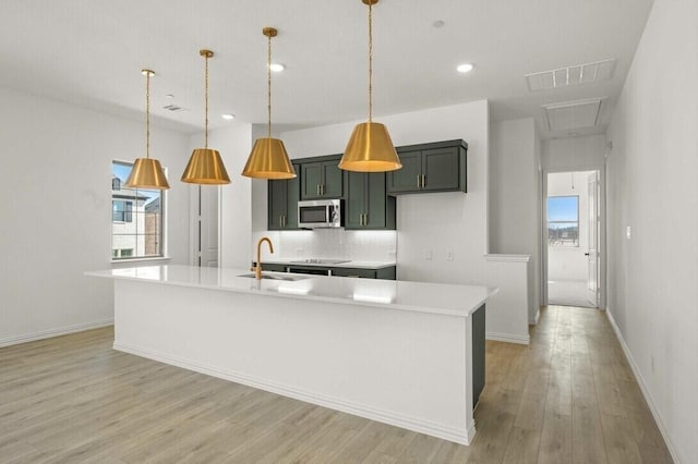 kitchen featuring light wood finished floors, visible vents, stainless steel microwave, light countertops, and a sink