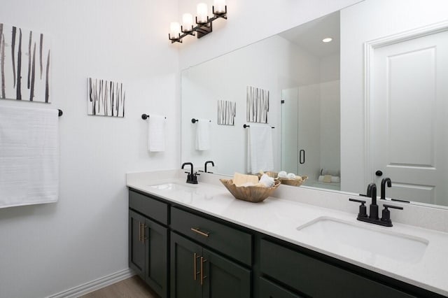 bathroom featuring double vanity, a stall shower, a sink, and baseboards