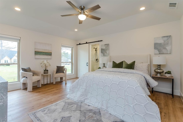 bedroom with a barn door, ceiling fan, and light hardwood / wood-style floors