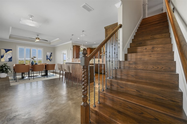 staircase featuring concrete flooring, crown molding, ceiling fan, and a tray ceiling