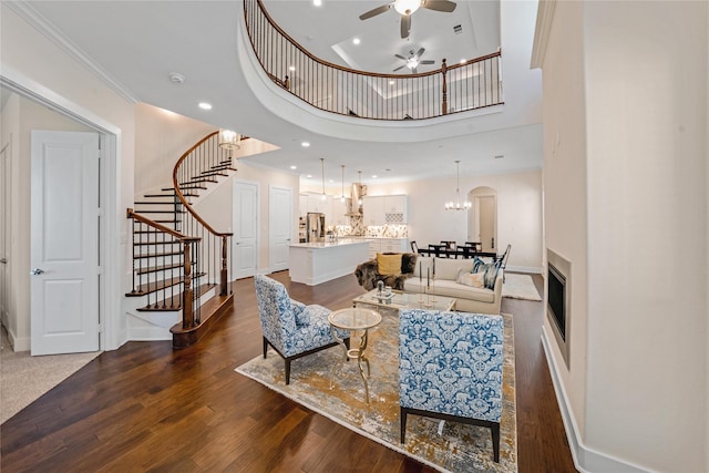 living room featuring a towering ceiling, dark wood-type flooring, ceiling fan with notable chandelier, and ornamental molding