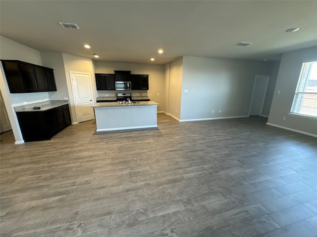 kitchen with light stone countertops, light wood-type flooring, a center island with sink, and sink