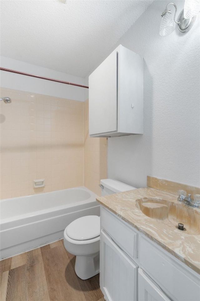 full bathroom featuring a textured ceiling, toilet, hardwood / wood-style flooring, vanity, and tiled shower / bath