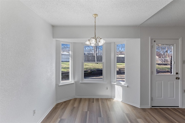 unfurnished dining area with a textured ceiling, light hardwood / wood-style flooring, a wealth of natural light, and an inviting chandelier