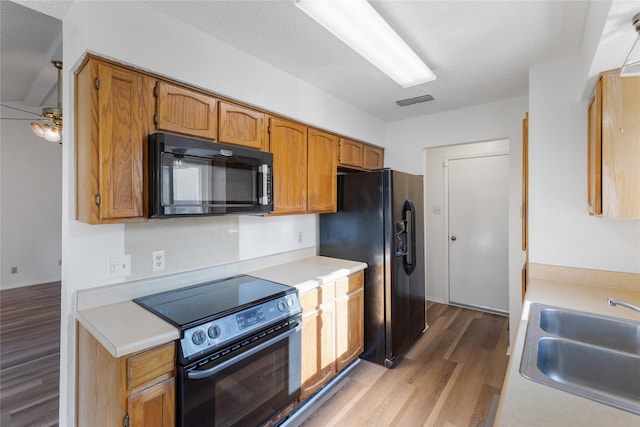 kitchen featuring sink, black appliances, a textured ceiling, and light hardwood / wood-style floors