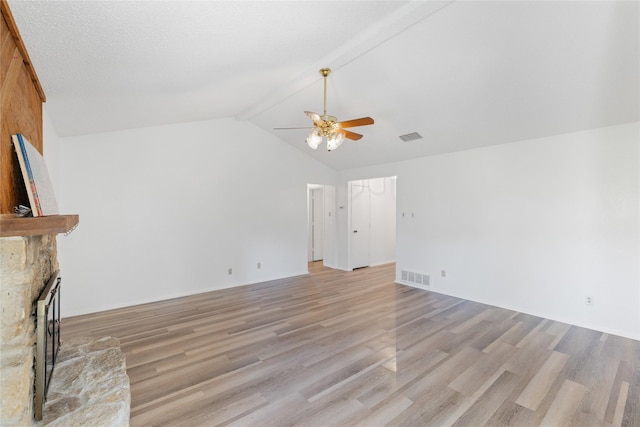 unfurnished living room with lofted ceiling with beams, light hardwood / wood-style floors, a stone fireplace, and ceiling fan