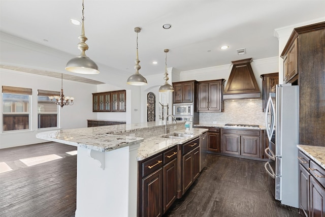 kitchen with pendant lighting, a large island with sink, custom exhaust hood, stainless steel appliances, and sink