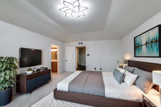 bedroom featuring a tray ceiling, ensuite bath, light carpet, and a notable chandelier