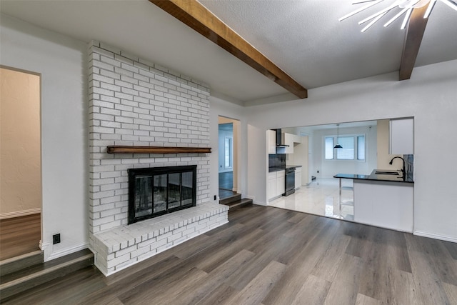 unfurnished living room featuring a textured ceiling, sink, beam ceiling, a fireplace, and light hardwood / wood-style floors