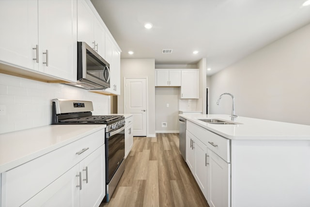 kitchen featuring white cabinetry, sink, stainless steel appliances, an island with sink, and light wood-type flooring