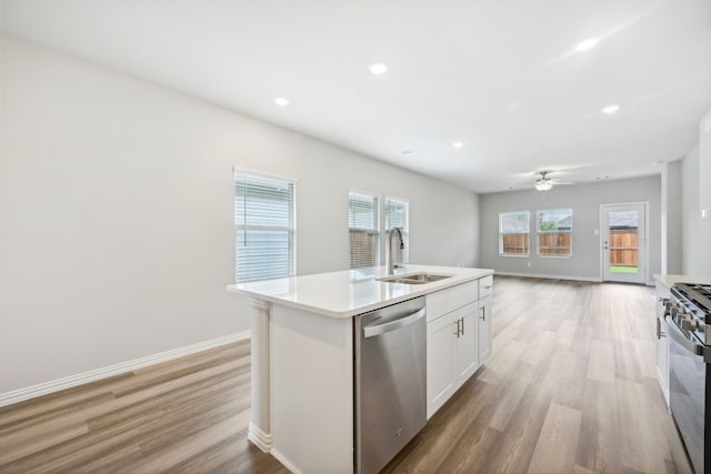 kitchen with appliances with stainless steel finishes, sink, light hardwood / wood-style floors, white cabinetry, and an island with sink