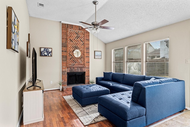 living room with a brick fireplace, a textured ceiling, ceiling fan, hardwood / wood-style flooring, and lofted ceiling