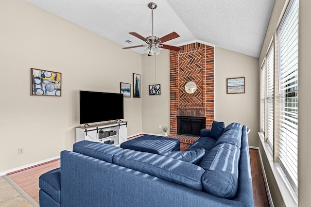 living room with ceiling fan, a brick fireplace, hardwood / wood-style floors, a textured ceiling, and vaulted ceiling