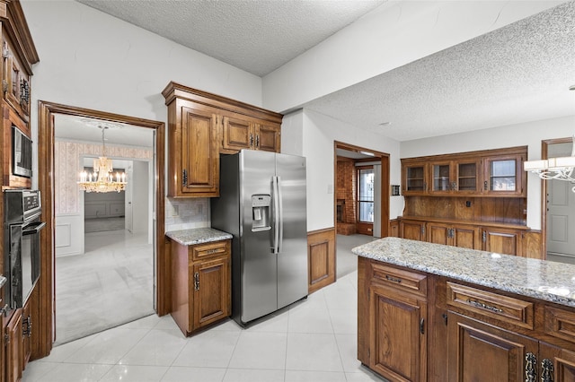 4247 Blackheath Rd, Dallas, TX 75227 - kitchen with light tile patterned flooring, oven, light stone counters, stainless steel fridge with ice dispenser, and an inviting chandelier