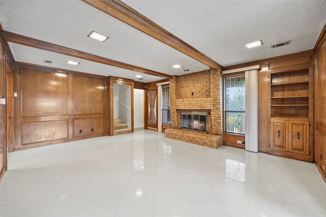 4247 Blackheath Rd, Dallas, TX 75227 - unfurnished living room featuring built in features, wooden walls, beamed ceiling, a brick fireplace, and a textured ceiling