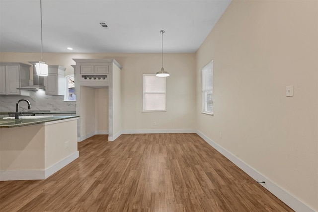 kitchen with gray cabinets, sink, backsplash, hanging light fixtures, and wall chimney exhaust hood