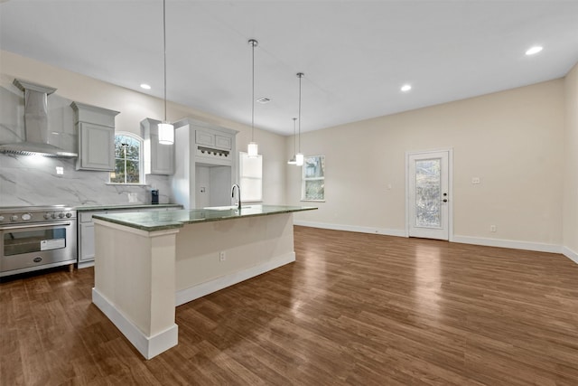 kitchen featuring stainless steel electric range oven, a center island with sink, wall chimney exhaust hood, and decorative light fixtures