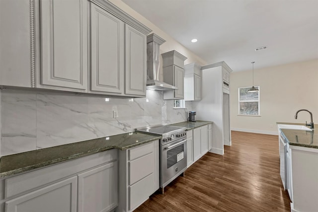 kitchen with stainless steel stove, sink, decorative backsplash, hanging light fixtures, and wall chimney exhaust hood