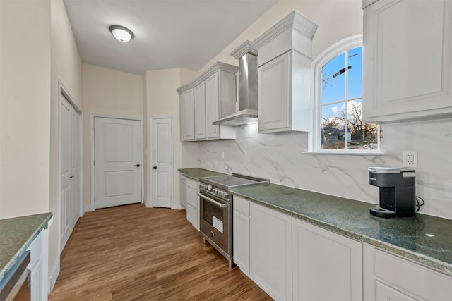 kitchen featuring light hardwood / wood-style flooring, high end stove, white cabinets, decorative backsplash, and wall chimney range hood