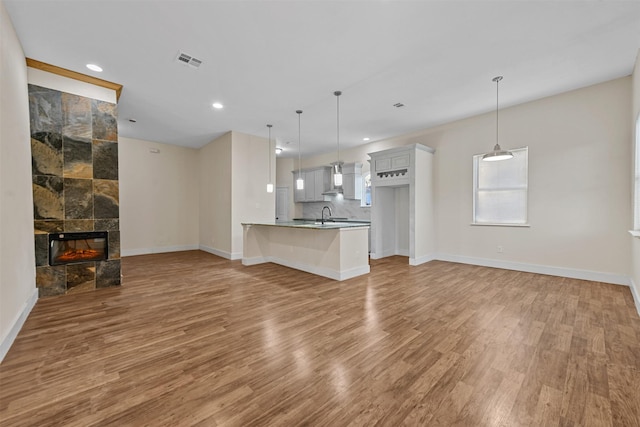 unfurnished living room with a tiled fireplace, sink, and light hardwood / wood-style floors