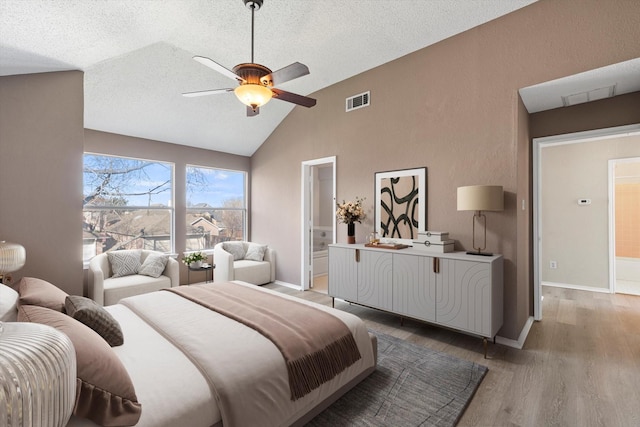 bedroom with vaulted ceiling, ensuite bath, ceiling fan, light wood-type flooring, and a textured ceiling