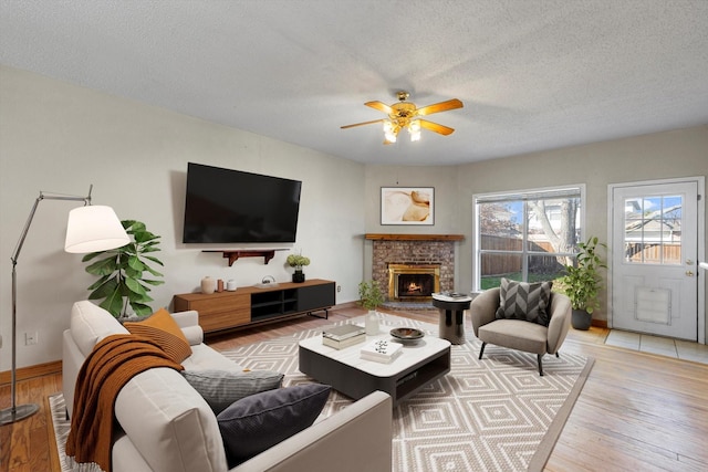 living room featuring ceiling fan, light hardwood / wood-style flooring, a textured ceiling, and a brick fireplace