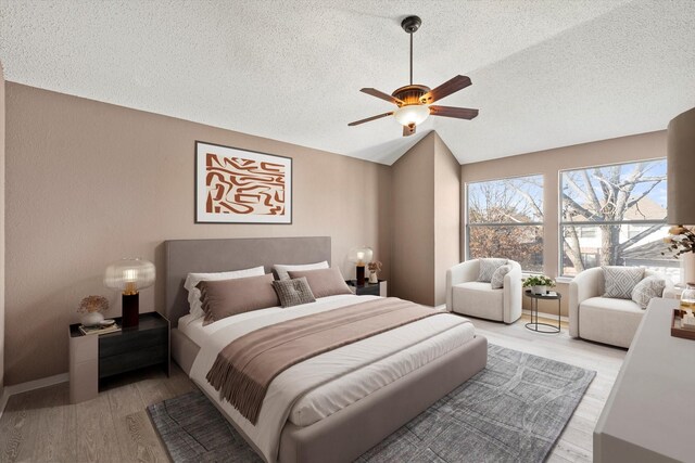 bedroom featuring ceiling fan, light hardwood / wood-style floors, lofted ceiling, and a textured ceiling