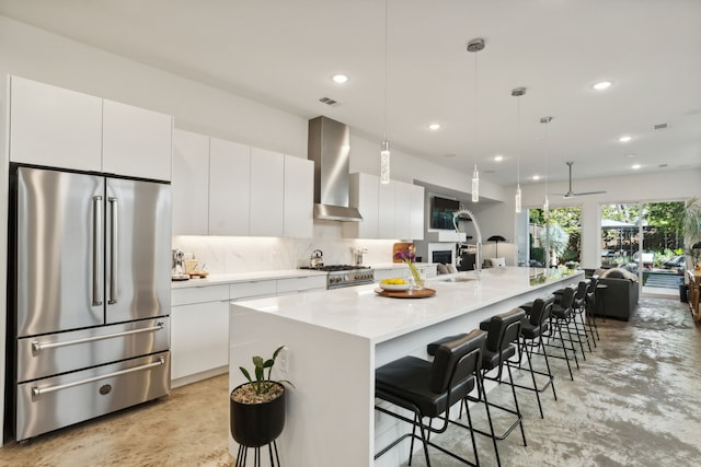 kitchen with wall chimney exhaust hood, white cabinetry, high quality appliances, and a kitchen island with sink