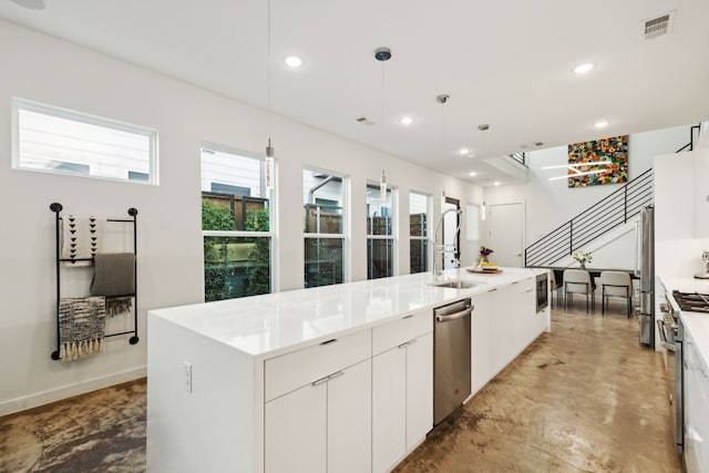 kitchen featuring stainless steel appliances, hanging light fixtures, a center island with sink, and white cabinets