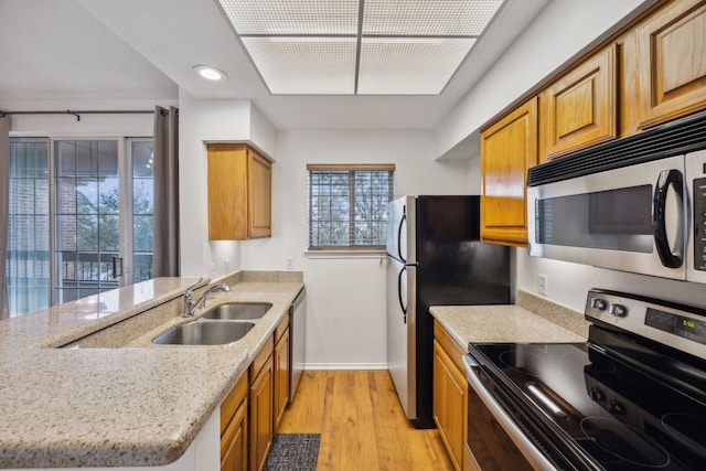 kitchen with sink, appliances with stainless steel finishes, light stone countertops, kitchen peninsula, and light wood-type flooring